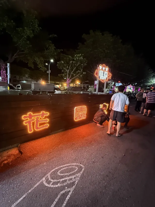 花園夜市外圍木圍籬上的花園霓虹字樣,後方是夜市附設的停車場與車輛