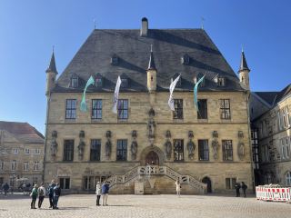 奧斯納布呂克(Osnabrück)位於德國下薩克森州西南部,毗鄰北萊茵-威斯特法倫州,距離荷蘭邊境約70公里,哈澤河(Hase)流經市區,人口約16萬,是下薩克森州第四大城市。其歷史可追溯至公元780年左右,查理曼大帝在此建立主教區,使其逐漸發展成為重要的宗教和商業中心。14世紀,奧斯納布呂克加入漢薩同盟,貿易日益繁榮;19世紀工業革命時期,鐵路建設帶動了機械製造、金屬加工和紡織等產業的發展。奧斯納布呂克主教座堂始建於9世紀,融合羅馬式和哥特式建築風格,內部珍藏著精美的宗教藝術品。老市政廳建於15世紀,是1648年《威斯特伐利亞和約》部分條約的簽署地。該和約結束了持續30年的歐洲三十年戰爭(1618—1648),奠定了近代國際關係的重要基礎。因此,奧斯納布呂克與明斯特(Münster)共同被譽為“和平之城”(Friedensstadt),併成為歐洲和平與外交歷史的重要象徵。