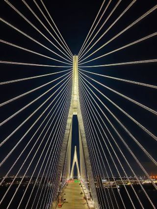 สำรวจทัศนียภาพริมแม่น้ำวินด์เซอร์ยามค่ำคืนอันน่าหลงใหล และพบกับแลนด์มาร์คที่จะพลิกโฉมประวัติศาสตร์การคมนาคมของอเมริกาเหนือ—สะพานนานาชาติกอร์ดี โฮว์! ทริปนี้ไม่ได้เป็นเพียงแค่การเยี่ยมชมสะพานแอมบาสซาเดอร์อันโด่งดังเท่านั้น สะพานเคเบิลแขวนสูงตระหง่านแห่งนี้สว่างไสวไปด้วยแสงไฟระยิบระยับ และการเดินเล่นริมแม่น้ำในยามค่ำคืน ชมเรือแล่นผ่านผืนน้ำ จะทำให้คุณดื่มด่ำไปกับทิวทัศน์เมืองอันน่าหลงใหลบนพรมแดนแห่งนี้ ยิ่งไปกว่านั้น คือโอกาสที่จะได้ข้ามสะพานเคเบิลแขวนที่ยาวที่สุดของอเมริกาเหนืออย่างอิสระในปี 2026 และได้เห็นผลลัพธ์อันงดงามจากการออกแบบทางวิศวกรรมเกือบสิบปี สถาปัตยกรรม แม่น้ำ และแสงไฟในยามค่ำคืน ผสานกันสร้างทิวทัศน์เมืองวินด์เซอร์ที่น่าจดจำ เปลี่ยนทริปของคุณให้เป็นการสำรวจเมืองอย่างแท้จริง

สะพานคลาสสิกที่แนะนำในวินด์เซอร์:

1. เยี่ยมชมสะพานแอมบาสซาเดอร์

📍ที่อยู่: 3500 Toledo St, Detroit, MI 48216-1079

⏰เวลาเปิดทำการ: เปิด 24 ชั่วโมง 7 วันต่อสัปดาห์ มานาน 365 ปีแล้ว

สะพานเก่าแก่สุดคลาสสิกแห่งนี้ที่เชื่อมระหว่างสหรัฐอเมริกาและแคนาดา ไม่ได้เป็นเพียงศูนย์กลางการคมนาคมเท่านั้น แต่ยังเป็นพยานถึงชีวิตและประวัติศาสตร์ของทั้งวินด์เซอร์และดีทรอยต์ ในเวลากลางวัน คุณจะได้สัมผัสบรรยากาศที่คึกคักของพื้นที่ชายแดน ในเวลากลางคืน คุณจะหลงใหลไปกับแสงสะท้อนของสะพานบนแสงไฟ ไม่ว่าจะขับรถหรือเดิน ที่นี่เป็นหนึ่งในจุดที่ดีที่สุดในการเก็บภาพทิวทัศน์ริมแม่น้ำ

2. ชมภาพกลางคืนของสะพานนานาชาติกอร์ดี โฮว์

แม้ว่าจะยังไม่เปิดอย่างเป็นทางการ แต่สะพานนานาชาติกอร์ดี โฮว์กำลังอยู่ในขั้นตอนสุดท้ายและคาดว่าจะเปิดในปี 2026 ทำให้คนเดินเท้า จักรยาน รถยนต์ และยานพาหนะอื่นๆ สามารถข้ามแม่น้ำได้ โครงการสุดล้ำนี้ดึงดูดผู้ชื่นชอบการถ่ายภาพนับไม่ถ้วนตั้งแต่เริ่มก่อสร้างในปี 2018 ตอนนี้ เมื่อมองจากฝั่งตรงข้ามในเวลากลางคืน การออกแบบแสงไฟของสะพานเริ่มเป็นรูปเป็นร่าง สร้างบรรยากาศที่ชวนฝันและโรแมนติกเมื่อรวมกับการล่องเรือในแม่น้ำ

▶️เคล็ดลับ: เพื่อให้ได้ชื่นชมความงามของสถาปัตยกรรมในเวลากลางคืนอย่างเต็มที่ แนะนำให้เลือกสถานที่ใกล้ริมฝั่งแม่น้ำที่มีทัศนียภาพกว้างไกล โดยเฉพาะในช่วงเวลาพลบค่ำหรือดึกดื่น

3. ประสบการณ์ล่องเรือในแม่น้ำยามค่ำคืน
วินด์เซอร์มีชีวิตชีวาในยามค่ำคืน แนะนำให้จองทัวร์ล่องเรือยามค่ำคืนเพื่อชื่นชมทิวทัศน์เมืองที่สว่างไสวด้วยแสงนีออนและสะพานต่างๆ ที่ผสานกันจากผืนน้ำ เรือจะให้บริการทัศนียภาพแบบพาโนรามาของสะพานทั้งสองแห่ง พร้อมด้วยอาหารว่างและเครื่องดื่มเบาๆ ให้คุณได้เพลิดเพลินไปกับสายลมเย็นๆ ของแม่น้ำ

▶️เคล็ดลับ: ทัวร์ล่องเรือยอดนิยมมักจะเต็มในช่วงฤดูท่องเที่ยว ดังนั้นการจองล่วงหน้าจึงเป็นสิ่งสำคัญ

🍽️คำแนะนำด้านอาหาร: หลังจากการล่องเรือยามค่ำคืน คุณสามารถหาบาร์หรือร้านอาหารริมฝั่งแม่น้ำได้ตามต้องการ ใจกลางเมืองวินด์เซอร์และทางเดินริมแม่น้ำมีร้านอาหารตะวันตกคุณภาพสูง บาร์ และอาหารแคนาดาแท้ๆ ให้เลือกมากมาย ตัวอย่างเช่น ร้าน The Keg Steakhouse & Bar (ที่อยู่: 31 Riverside Dr E, Windsor, ON N9A 2S4) เป็นสถานที่ยอดนิยมสำหรับคนท้องถิ่นในช่วงดึก

คำแนะนำการเดินทาง: จากใจกลางเมืองวินด์เซอร์ไปยังสะพานแอมบาสซาเดอร์ แนะนำให้ขับรถหรือนั่งแท็กซี่ (ประมาณ 10-15 นาที) หากเริ่มต้นจากใจกลางเมืองวินด์เซอร์ คุณสามารถนั่งรถทัวร์หรือเดินเลียบแม่น้ำเพื่อหาจุดชมวิวที่เหมาะสมได้

รถประจำทางสาธารณะส่วนใหญ่ในวินด์เซอร์ให้บริการจนถึงประมาณ 23:00 น. หากคุณวางแผนที่จะเดินเล่นริมฝั่งแม่น้ำในเวลากลางคืน แนะนำให้เผื่อเวลาสำหรับการเดินทางกลับด้วยแท็กซี่

เคล็ดลับการเดินทางที่ใช้งานได้จริง: ในปี 2026 ไม่ว่าคุณจะเลือกเดิน ปั่นจักร หรือขับรถ คุณก็จะได้ข้ามสะพานเคเบิลที่ยาวที่สุดแห่งหนึ่งในอเมริกาเหนือ! เมื่อการก่อสร้างใกล้เสร็จสมบูรณ์ ผู้ที่ชื่นชอบสถาปัตยกรรม การคมนาคม หรือการถ่ายภาพ สามารถวางแผนล่วงหน้าเพื่อเก็บภาพสะพานทั้งหลังและเป็นสักขีพยานในยุคใหม่แห่งการแลกเปลี่ยนระหว่างสองประเทศ สถานที่ที่ไม่ควรพลาดในอนาคต: กอร์ด