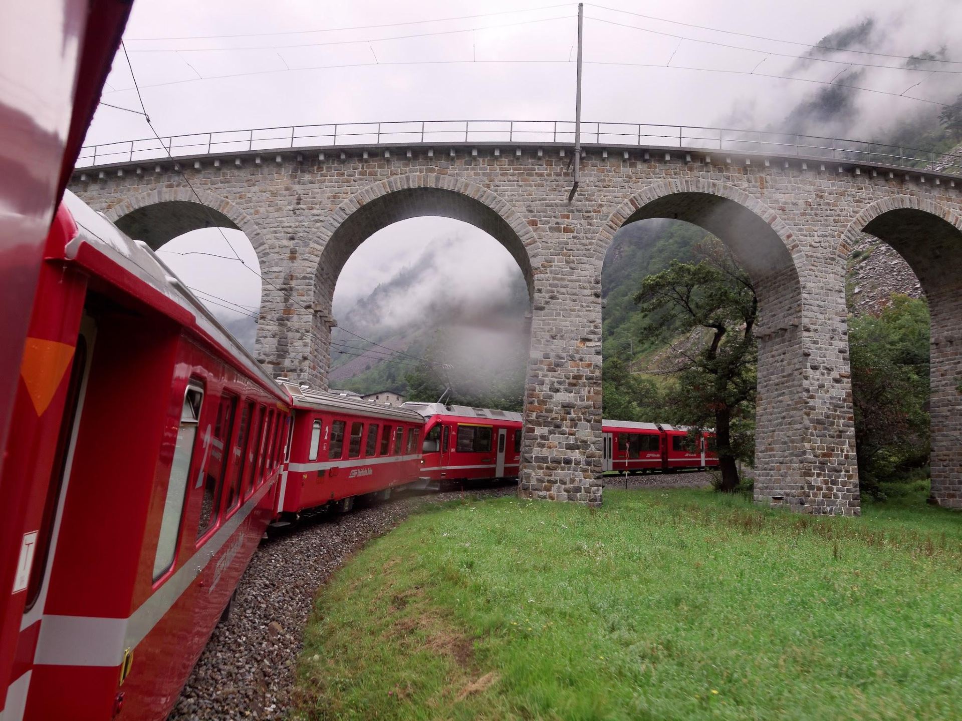 🚂 From Glaciers to Palm Trees: Why the Bernina Express Is the World’s Most Scenic Rail Journey!

Recognized as a UNESCO World Heritage railway, the Bernina Express operated by the Rhaetian Railway (RhB) is widely regarded as one of the most spectacular train journeys on Earth. Connecting Chur or St. Moritz in Switzerland to Tirano in northern Italy, this red panoramic train conquers dramatic alpine passes without the use of a cogwheel track.

Traversing 55 tunnels, 196 bridges, and soaring up to 2,253 meters above sea level at the Ospizio Bernina pass, the route delivers a breathtaking contrast: journeying from snow-capped glacial peaks and granite gorges to the sun-soaked vineyards and palm-lined piazzas of Italy in just over four hours.




Marvel at the Landwasser Viaduct: One of the most famous railway bridges in the world, this 65-meter-high curved limestone viaduct plunges directly into a sheer rock cliff tunnel. The massive panoramic windows offer a stunning vantage point as the bright red train curves along the slender stone arches.

Stand in Awe of the Morteratsch & Palü Glaciers: As the train ascends into the high Engadin alpine pass, gaze out at the vast white expanse of the Morteratsch Glacier and the turquoise waters of Lago Bianco, framed by the jagged summits of the Bernina Range.

Spiral Down the Brusio Circular Viaduct: Near the Italian border, the train navigates a dramatic 360-degree open-air spiral stone viaduct built entirely above ground. The looping track allows the train to drop elevation smoothly while offering passengers a full view of the front and rear train cars.

Stop at Alp Grüm for Glacial Panoramas: Accessible only by rail or foot, this scenic high-mountain railway station sits perched on a cliff ledge, offering uninterrupted views down into the Val Poschiavo and up toward the hanging Palü Glacier.

Arrive for Gelato & Wine in Tirano: Crossing the border into Italy, the train rolls right through town streets to terminate in Tirano. Spend time exploring the Renaissance Basilica of Madonna di Tirano and relaxing in sunlit cobblestone squares with authentic pasta, Valtellina wine, and gelato.

💡 Essential Travel Tips

Best Time to Travel:

Summer (June–September): Perfect for clear panoramic views, emerald alpine lakes, blooming valleys, and warm Italian terrace dining.

Winter (December–March): A genuine winter wonderland where frozen lakes, snowdrifts piled high at the pass, and frosted pine forests create a magical landscape.

Seat Reservations vs. Regional Trains:

The official Bernina Express panoramic cars require a seat reservation fee in addition to a valid ticket or rail pass.

Blogger tip: Local regional trains (marked "R" or "RE") run the exact same tracks on an hourly schedule. They do not require seat reservations, and their windows can be pulled down for glare-free photography.

Pass Validity: The entire route is fully covered by the Swiss Travel Pass and Eurail Pass (reservation fees for the official