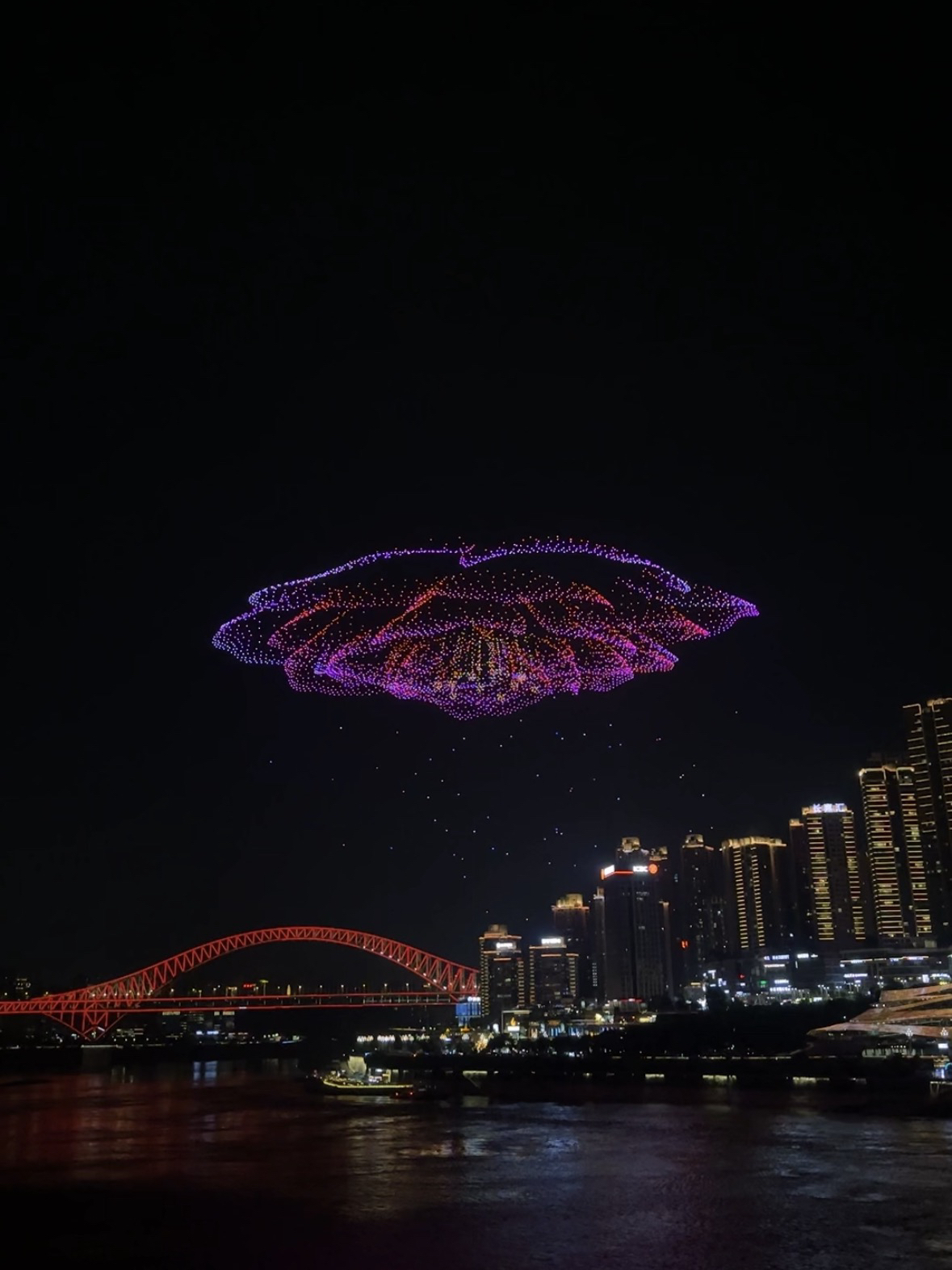 Jika perjalanan Anda ke Chongqing bertepatan dengan Pertunjukan Drone Chongqing, pastikan untuk meluangkan satu malam untuk menontonnya. Ini adalah salah satu pertunjukan gratis terbesar di Tiongkok: ratusan drone secara bersamaan terbang ke langit, menciptakan tampilan cahaya yang luar biasa di atas gedung pencakar langit dan pertemuan dua sungai.

🕘 Jam berapa pertunjukan dimulai?

Pertunjukan biasanya berlangsung pada hari Sabtu pukul 21.00, tetapi selama kunjungan kami di Chongqing, pertunjukan ditunda hingga hari Rabu karena ujian sekolah. Untuk informasi terbaru, silakan periksa akun WeChat resmi "重庆发布" (Siaran Pers Chongqing) atau situs web pemerintah Chongqing.

Sebaiknya tiba paling lambat pukul 20.00–20.15, terutama jika Anda ingin mendapatkan tempat yang bagus di tepi sungai. Semakin dekat Anda ke pertunjukan, semakin ramai, dan beberapa tempat populer akan penuh sesak.

Pertunjukan berlangsung sekitar 15–20 menit, tetapi pengalamannya jauh lebih lama.

📍 Tempat Menonton Terbaik

Menurut kami, tempat terbaik adalah:

📌 Tepi sungai dekat Raffles City - di sinilah kami menonton.

📌 Taman Perbelanjaan Changjiahui - tempat ini menawarkan perspektif berbeda tentang pusat kota Chongqing. Biasanya agak kurang ramai, dan foto-fotonya sangat atmosferik. Drone lepas landas dari sini.

📌 Jembatan Chaotianmen - pilihan bagus jika Anda ingin menonton pertunjukan dari atas dan melihat lebih banyak panorama kota.

📌 Jembatan Qiansimen - titik pandang luar biasa lainnya dengan pemandangan pusat kota dan sungai.

💡 Tips

· Sebaiknya datang lebih awal - sekitar 45-60 menit sebelum pertunjukan dimulai.

· Periksa jadwal terlebih dahulu di akun WeChat resmi "重庆发布" (Siaran Pers Chongqing) atau di situs web pemerintah Chongqing. Harap dicatat bahwa pertunjukan akan dibatalkan jika cuaca buruk. • Jangan langsung bergegas pergi setelah pertunjukan berakhir – antrean panjang terbentuk di pintu keluar kereta bawah tanah dan taksi. Lebih baik berjalan-jalan di sepanjang tepi sungai selama 20-30 menit.

✨ Ringkasan

Jika Anda berada di Chongqing pada hari pertunjukan, pastikan untuk memasukkannya ke dalam rencana perjalanan Anda. Ini adalah pertunjukan yang sepenuhnya gratis, tetapi skalanya setara dengan banyak pertunjukan berbayar.

Bagi kami, itu adalah penutup yang sempurna untuk hari kami di Chongqing. Tampilan cahaya yang sangat besar di atas gedung pencakar langit, pantulan cahaya di sungai, dan suasana kota di malam hari menjadikannya salah satu malam yang paling berkesan selama perjalanan kami ke Tiongkok.