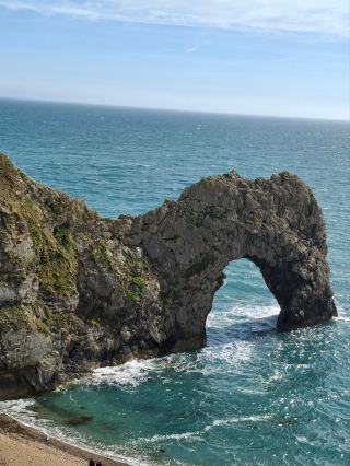 Durdle Door

The form of the coastline around Durdle Door is controlled by its geology—both by the contrasting hardnesses of the rocks, and by the local patterns of faults and folds. The arch has formed on a concordant coastline where bands of rock run parallel to the shoreline. The rock strata are almost vertical, and the bands of rock are quite narrow. Originally a band of resistant Portland limestone ran along the shore, the same band that appears one mile along the coast forming the narrow entrance #durdledoor to Lulworth Cove. Behind this is a 120-metre (390 ft) band of weaker, easily eroded rocks, and behind this is a stronger and much thicker band of chalk, which forms the Purbeck Hills. These steeply dipping rocks are part of the Lulworth crumple, itself part of the broader Purbeck Monocline, produced by the building of the Alps during the mid-Cenozoic.