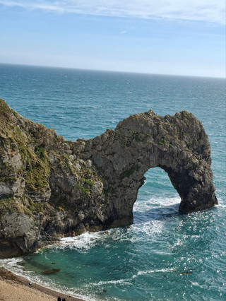Durdle Door
The form of the coastline around Durdle Door is controlled by its geology—both by the contrasting hardnesses of the rocks, and by the local patterns of faults and folds. The arch has formed on a concordant coastline where bands of rock run parallel to the shoreline. The rock strata are almost vertical, and the bands of rock are quite narrow. Originally a band of resistant Portland limestone ran along the shore, the same band that appears one mile along the coast forming the narrow entrance #durdledoor to Lulworth Cove. Behind this is a 120-metre (390 ft) band of weaker, easily eroded rocks, and behind this is a stronger and much thicker band of chalk, which forms the Purbeck Hills. These steeply dipping rocks are part of the Lulworth crumple, itself part of the broader Purbeck Monocline, produced by the building of the Alps during the mid-Cenozoic.