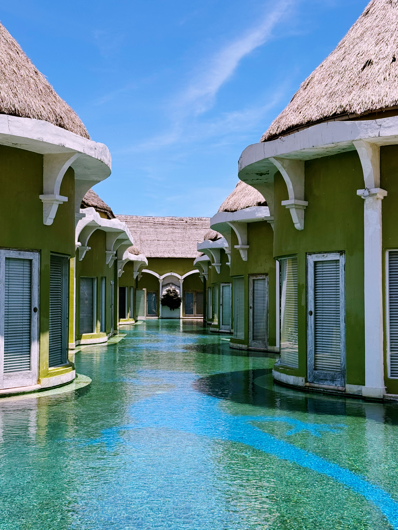 
Saya baru saja menemukan *hidden gem* di mana Anda bisa langsung melangkah dari ruang tamu ke laguna yang sebening kristal. Villa Seminyak Estate & Spa adalah oasis luar biasa yang tersembunyi dari hiruk pikuk jalan utama. Nilai estetika yang rapi dari vila beratap jerami yang berpadu dengan air berwarna biru kehijauan ini benar-benar memanjakan mata. Ini adalah tempat paling sempurna untuk sejenak menjauh dari rutinitas dan menikmati suasana pulau yang santai. Bangun tidur dengan pemandangan air tepat di depan pintu memberikan kesan mistis yang magis, rasanya seperti hidup di dalam mimpi tropis. Pelarian yang benar-benar menenangkan jiwa bagi siapa saja yang mencari pengalaman menginap unik di Bali.
Info Bermanfaat
Lokasi: Jl. Nakula, Gang Baik-Baik, Seminyak.
Harga: $120 - $250 per malam.
Waktu Terbaik: Musim kemarau (Mei-September) untuk menikmati momen bersantai di tepi kolam.
Tips Ahli
Pastikan untuk memesan Lagoon Villa jika Anda ingin mendapatkan akses langsung ke air. Manfaatkan layanan antar-jemput gratis mereka untuk pergi ke pantai atau Seminyak Square tanpa harus lelah berjalan kaki!
Alasan berkunjung
Kesempatan langka untuk menginap di vila "terapung" tepat di jantung Seminyak.