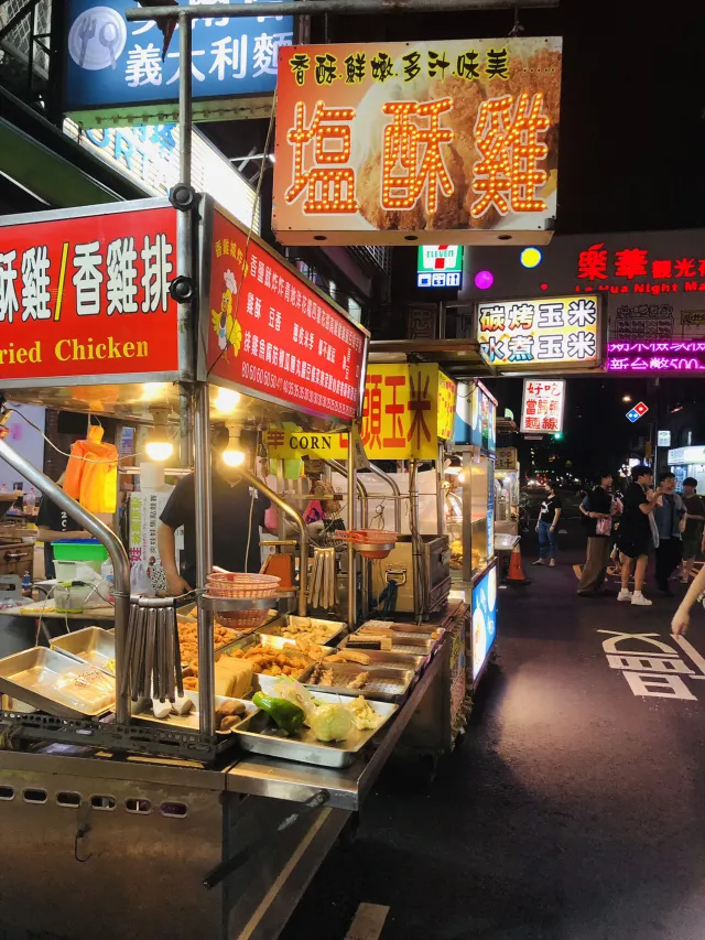 樂華夜市的攤位街景,碳烤玉米、水煮玉米與炸物攤沿著走道排開,燈光明亮人潮不斷