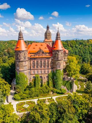 The highlighted building is Książ Castle (Zamek Książ), famously known as the "Pearl of Lower Silesia," located in Wałbrzych, Poland. Built between 1288 and 1292 by Duke Bolko I the Strict, it stands as the third-largest castle in Poland and the largest fortress in the Silesia region.
The castle is spectacularly situated on a steep rock cliff within the protected Książ Landscape Park, overlooking the Pełcznica River Gorge.
For over 400 years, the castle belonged to the prominent Hochberg family, who transformed it from a medieval fortification into a sprawling, eclectic palace boasting over 400 rooms.Architectural Eclecticism: Due to centuries of restructuring, it beautifully fuses Gothic, Renaissance, Baroque, and Neo-Romanesque styles.World War II Secrets: Seized by Nazi forces during the war, the castle was heavily modified to serve as a headquarters for Adolf Hitler. It hides a mysterious network of underground tunnels carved deep into the rock as part of the top-secret Project Riese.
 Terraced Gardens: The lush manicured lawns shown in the foreground span 14 distinct terraces, designed by English gardeners to drape elegantly down the cliffside.The Underground Tunnels: Visitors can take a dedicated guided route to explore 1.5 kilometers of concrete-reinforced wartime tunnels beneath the estate.The Palm House (Palmiarnia): Located just a short distance from the fortress, this historic greenhouse is filled with exotic, tropical plants.Sightseeing Hours: Generally open daily from 9:00 AM to 6:00 PM during high season (April to October), with slightly reduced hours in winter.