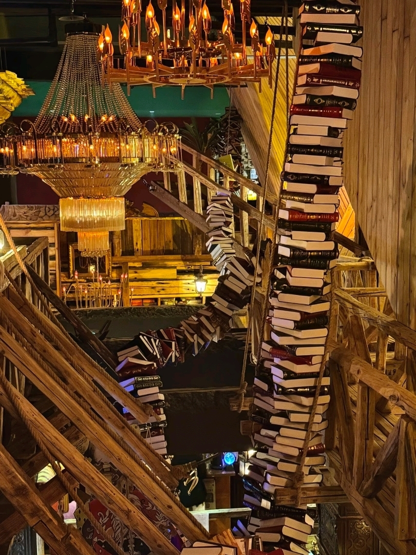 Harbin isn't just about snow; it hides a "magical world" within. On that day, while strolling along Central Avenue (中央大街) amidst the freezing temperatures and biting cold wind, I turned into a small alley. Suddenly, it felt like a portal to another dimension had opened. There, I found old wooden stairs, raw wooden beams, the scent of wood mixed with warm coffee, and books stacked as if floating in mid-air. Wow... this isn't just an ordinary café; it's like a scene from a magical school. Warm golden lights cast shadows of books on wooden walls, and every corner is picture-perfect, especially the "spiraling floating books" spot—it's the highlight!

Let the freezing cold stay outside because inside, it's warm and cozy like old Europe. Soft conversations and gentle background music make it feel like you're in a novel. This unexpected surprise turned out to be the best moment of the trip.

📍 Location
Central Avenue, Harbin
Known by locals as:
“中央大街哈利波特魔法屋”
Located in a small alley near the main street (around No. 37).

💰 Approximate Prices
Drinks: 35–60 yuan
Snacks: 30–50 yuan
(Reasonable for a themed café in a tourist area.)

⏰ Best Time to Visit
Evening to night (the lights are stunning).
Winter is the best season as it's cold outside but warm inside.

🚶♀️ How to Get There
Stay in the Central Avenue area and walk there.
Or call a Didi to "中央大街" and walk into the alley.