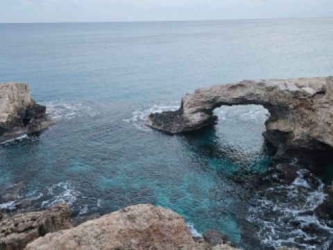 Fall in Love With Ayia Napa’s Bridge of Love 🌊🌅💙  
If you’re chasing breathtaking natural wonders, the Bridge of Love in Ayia Napa is a must-see! This iconic rock arch perched above shimmering turquoise waters is the kind of spot that makes you feel like you’ve stepped into a postcard—especially as the sunset paints the sky in glowing pinks and golds.  

Here’s how to soak up the magic:  
Start your visit in the late afternoon to enjoy the warm glow on the arches, then snag the best photo spots from the edge of the cliffs (look for angles where the arch frames the sea). Dip your toes in the crystal-clear water below if the tide and weather allow—just be cautious with slippery rocks and wear sturdy sandals for extra grip. As evening arrives, the whole scene becomes truly “insta-worthy,” with the cliffs and natural arch glowing against the horizon—sunset here is unforgettable, so don’t rush off!  

📝 Practical Tips:  
- Address: X2M8+5M, Ayia Napa 5330, Cyprus  
- There’s no entrance fee or fixed opening hours—come any time, but sunset is the golden hour for both romance and photography!  
- The surrounding area is all-natural, so bring your own water and snacks, plus a trash bag to keep it pristine.  
- The terrain is rocky: keep an eye out for uneven ground and don’t get too close to the cliff edge, especially if windy.  

Personal insight: If you want the arch to yourself, try a weekday visit and be patient—sometimes group photoshoots happen, but the wait is totally worth it.  

#AyiaNapa #BridgeOfLove #CyprusTravel #NatureVision #SeasideAdventure