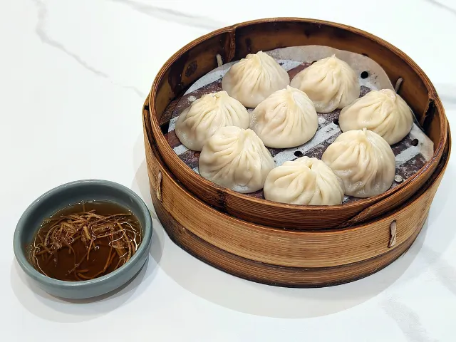Xiaolongbao in a basket next to ginger vinegar sauce