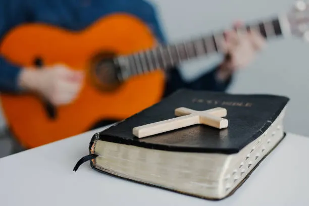 Close up Alkitab Kristen di atas meja kayu dengan laki-laki muda bermain gitar
