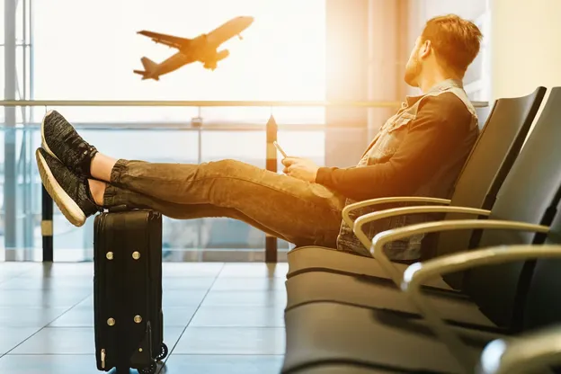 Man sitting at airport with legs on suitcase