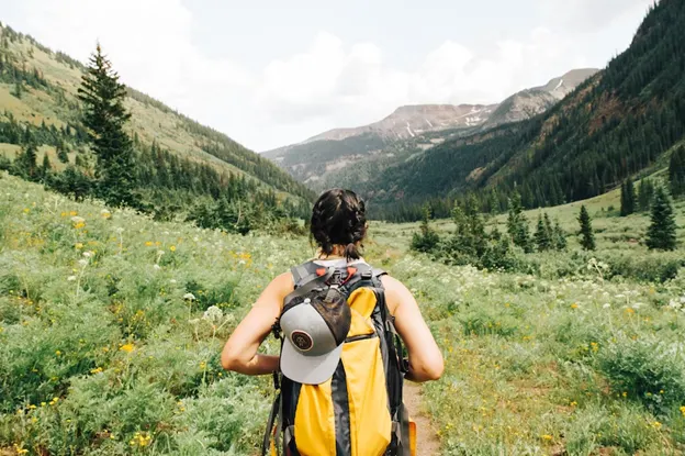 Woman with backpack in a field looking at mountains in the distance