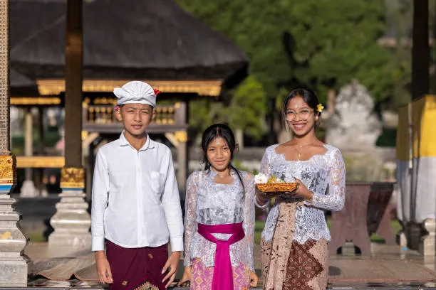 Keluarga Bali mengenakan pakaian adat, berdiri di pintu masuk sebuah pura