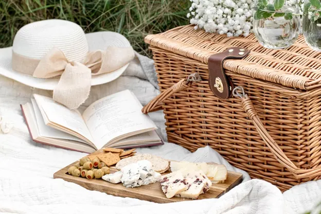 A picnic basket, white hat, book, and charcuterie board