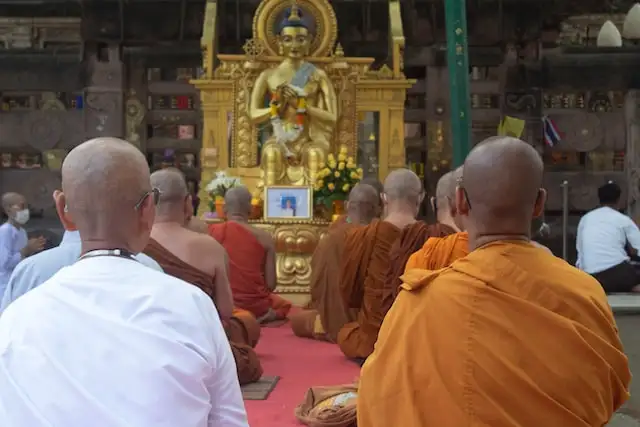 A group of monks chants in front of an image of Buddha