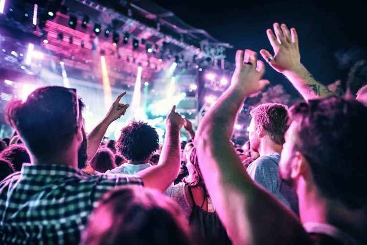 Crowd with raised hands at Creamfields festival, facing a brightly lit stage with pink and purple lights.