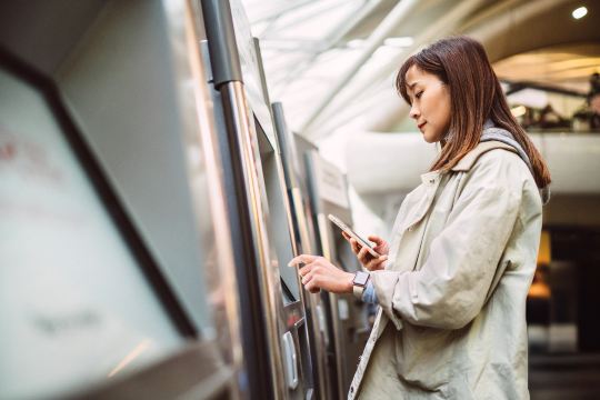Woman checking midweek train prices on phone at station.