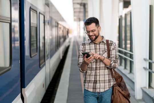 Man checking UK train ticket release on phone at platform.