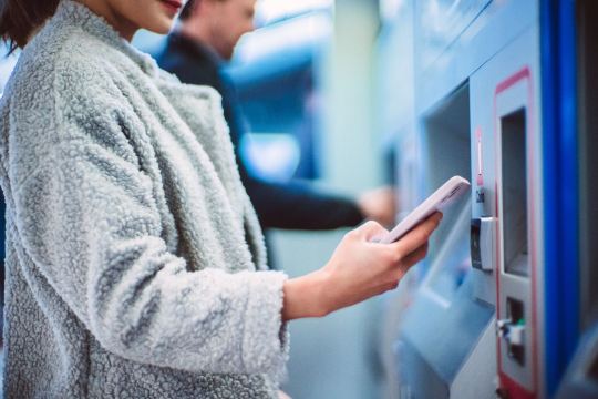 Woman buying flexible train ticket at station machine.