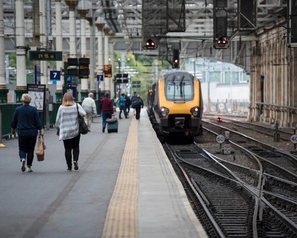 Passengers on platform with delayed train approaching station.
