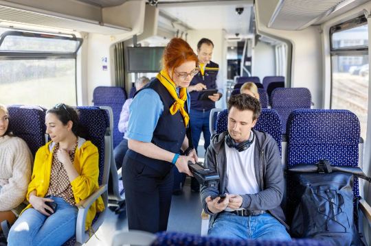 Train conductor checking tickets from seated passengers.