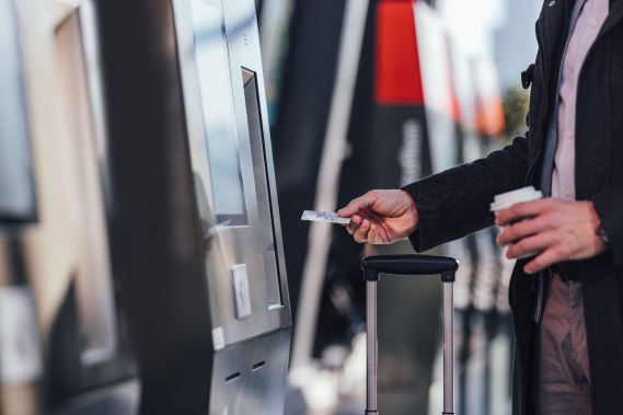 Man buying train ticket at station machine with luggage.