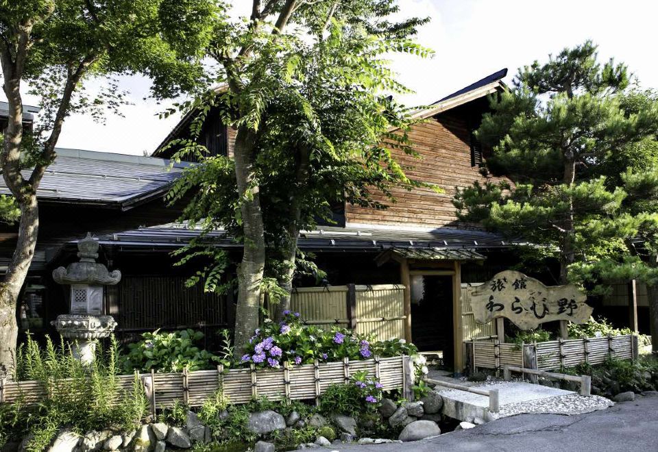 a wooden house with a large tree in front of it , surrounded by a garden at Ryokan Warabino