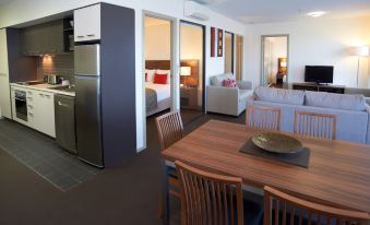 a modern kitchen and dining area with a refrigerator , wooden chairs , and a large mirror at Quest Werribee