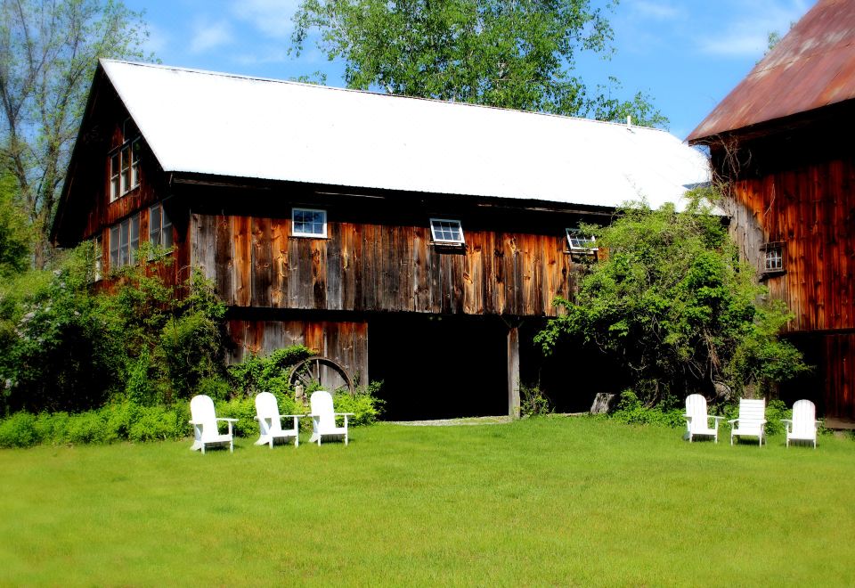 a wooden barn with a white roof , surrounded by lush green grass and white lawn chairs at Colby Hill Inn