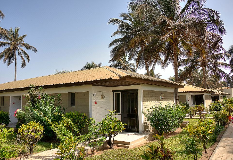 a small white house with a red tile roof is surrounded by palm trees and other greenery at Sunset Beach Hotel