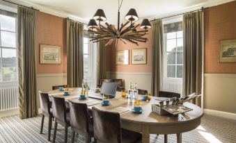 a dining room with a large wooden table surrounded by chairs , and a chandelier hanging above at The Painswick
