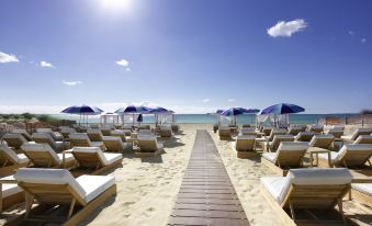 a sandy beach with numerous sun loungers and umbrellas , providing a comfortable setting for people to relax at Hard Rock Hotel Ibiza