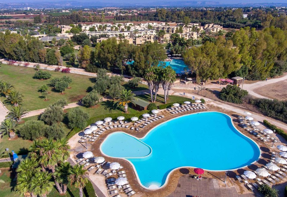 a large outdoor pool surrounded by lush greenery , with a view of the surrounding area at VOI Arenella Resort