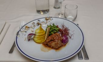 a plate of food with a steak and vegetables , garnished with a red sauce and a pear , is presented on a table at Hotel Petit Palais
