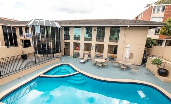 a large swimming pool is surrounded by a building and lounge chairs , with umbrellas and tables at Twin Towers Inn