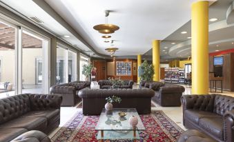 a large , well - lit room with multiple brown leather couches and chairs arranged around a glass coffee table at B&B Hotel Affi - Lago di Garda