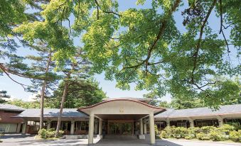 a large building surrounded by trees , with a covered walkway leading up to the entrance at Karuizawa Prince Hotel East