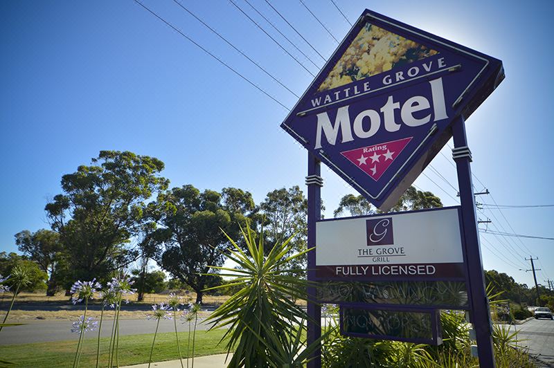 a motel with a large sign in front of it , surrounded by trees and grass at Wattle Grove Motel