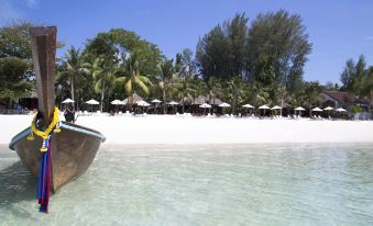 a boat is docked on a sandy beach near a body of water , with palm trees in the background at Mali Resort Pattaya Beach Koh Lipe