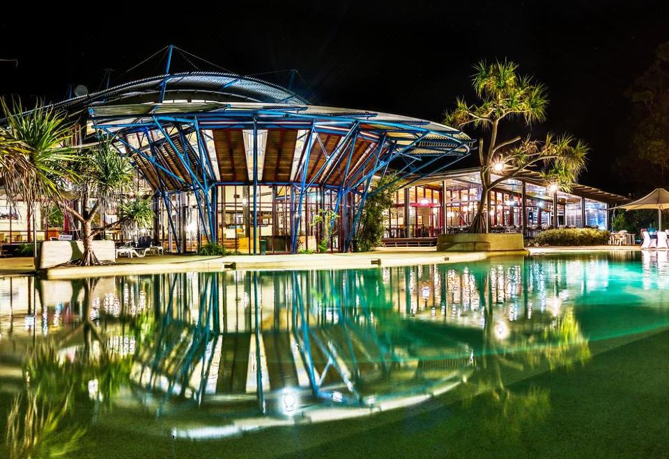 a modern building with a unique curved roof is reflected in the water , creating a tranquil atmosphere at Kingfisher Bay Resort