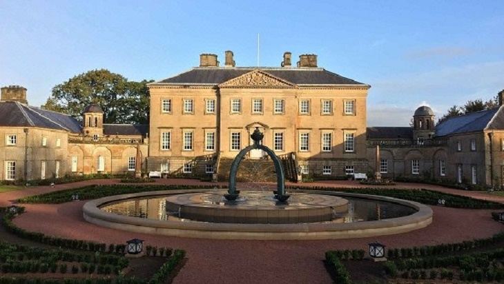 a large , beige - colored building with a fountain in front and trees surrounding it , under a clear blue sky at Ardwell Bed & Breakfast