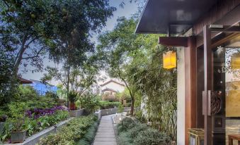 There is a garden with trees and plants in front, along the walkway leading to an outdoor room at West Lake Teavilla