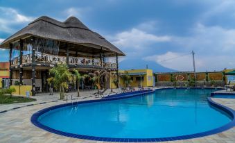 a large swimming pool with a thatched roof building in the background and mountains in the background at Fatima Hotel