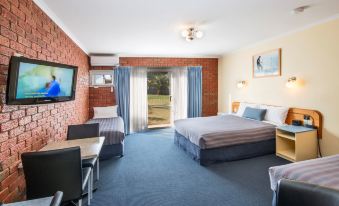 a hotel room with a bed , desk , and chairs , as well as a balcony overlooking the ocean at Torquay Tropicana Motel