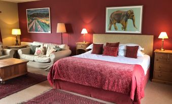 a luxurious bedroom with a king - sized bed , red curtains , and a couch , along with a painting on the wall at The Durham Ox