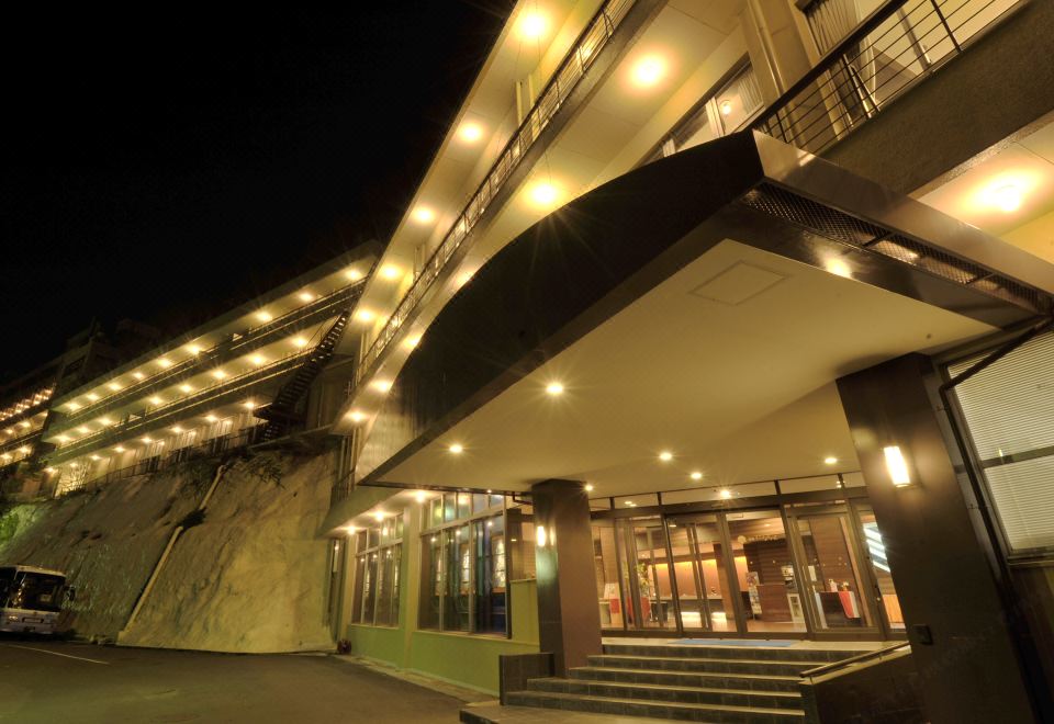 a nighttime view of a building with multiple levels and balconies , illuminated by lights against the dark sky at Nagasaki Nisshokan