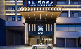 There is a hotel entrance with an illuminated sign above it, and there is another building in front of it at Kasion Pusham Hotel