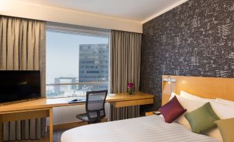 The bedroom features a double bed, desk, and a large window with a city view at Novotel Century Hong Kong