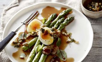 a plate of asparagus and a bowl of sauce with an egg on top are placed on a wooden table at Capri by Fraser Brisbane