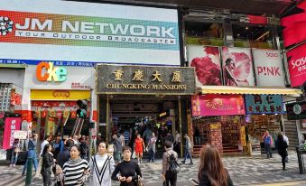 A crowd walks down the street in front of various buildings adorned with signs, as people pass by at Hong Kong Budget Hostel